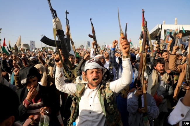 Houthi fighters brandish weapons during a protest following U.S. and British forces strikes, in the Houthi-controlled capital of Sanaa, Jan. 12, 2024.