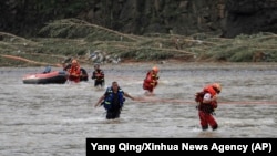 In this photo released by Xinhua News Agency, rescuers walk across a river after delivering relief items to affected people on the other bank in Heishanke Township, the city of Huludao in Liaoning province, Aug. 21, 2024. 