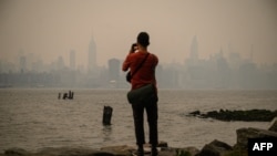A man stands before the New York city skyline and east river shrouded in smoke, in Brooklyn, June 6, 2023. Smoke from the hundreds of wildfires blazing in eastern Canada has drifted south.