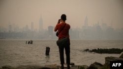 A man stands before the New York city skyline and east river shrouded in smoke, in Brooklyn, June 6, 2023. Smoke from the hundreds of wildfires blazing in eastern Canada has drifted south. 