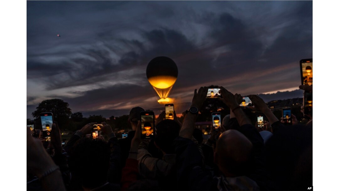 A crowd takes photos at the gates to the Tuileries Garden as the cauldron rises at sunset during the 2024 Summer Olympics, July 27, 2024, in Paris.