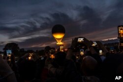 A crowd takes photos at the gates to the Tuileries Garden as the cauldron rises at sunset during the 2024 Summer Olympics, July 27, 2024, in Paris.