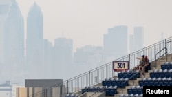 2023年6月8日，费城“费城人队”和底特律“老虎队”在公民银行公园举行的棒球比赛之前，两名球迷望向被加拿大野火的烟雾所掩盖的费城市中心。（《今日美国报》体育版照片）