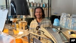 Anteneh Mulu, 46, poses behind the counter after serving a customer at his coffee shop, The Ethiopian Coffee Company, in central London on Thursday, Aug. 31, 2023. (AP Photo/Almaz Abedje)
