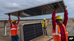 Workers carry a solar panel for installation at the under-construction Adani Green Energy Limited's Renewable Energy Park in the salt desert of Karim Shahi village. (AP Photo/Rafiq Maqbool)