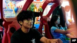 The Rev. Ai Hironaka, center, watches as his son Hoken, 17, left, and daughter Ayumu, 15, play a racing game at the Fun Factory in the Maui Mall, July 7, 2024, in Kahului, Hawaii.