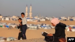 Seorang perempuan Palestina tampak membaca Al-Qur'an di dekat kamp pengungsi di Rafah, pada hari pertama bulan Ramadan pada 11 Maret 2024. (Foto: AFP/Mohammed Abed)