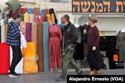 Un militar armado con su fusil reglamentario va de compras por una céntrica avenida de Jerusalén.