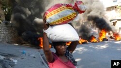 A woman walks past burning tires set on fire by protesters to call attention to the country's insecurity and demanding the resignation of the prime minister, in Port-au-Prince, Haiti, Jan. 18, 2024. 