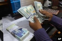 FILE - A Pakistani money trader counts U.S. dollars for a customer at a currency exchange office, in Karachi, Pakistan, May 19, 2022. Pakistan’s currency had plummeted against the U.S. dollar amid uncertainty about the success of crucial talks between the International Monetary Fund.