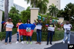 Protesters holding Haitian national flags and handmade signs with messages demanding Haiti's Prime Minister Ariel Henry resign, gather outside of the Marriott Hotel where they believe Henry is staying, in San Juan, Puerto Rico, March 6, 2024.