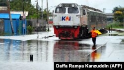 Seorang petugas memandu kereta api melewati jalur yang tergenang banjir di Semarang, Jawa Tengah, 5 Februari 2021. (Foto: Daffa Ramya Kanzuddin/AFP)