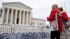 Two women stand outside the Supreme Court, where signs in the shape of grave headstones, with information on people who died from using OxyContin, line a security fence, in Washington, Dec. 4, 2023.
