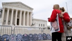 Two women stand outside the Supreme Court, where signs in the shape of grave headstones, with information on people who died from using OxyContin, line a security fence, in Washington, Dec. 4, 2023.