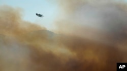 A firefighting airplane flies above clouds of smoke from a wildfire burning near houses in Alcabideche, outside Lisbon, Tuesday, July 25, 2023.