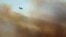A firefighting airplane flies above clouds of smoke from a wildfire burning near houses in Alcabideche, outside Lisbon, Tuesday, July 25, 2023.