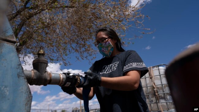 FILE - Raynelle Hoskie attaches a hose to a water pump to fill tanks in her truck outside a tribal office on the Navajo reservation, April 20, 2020, in Tuba City, Arizona.