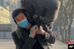 A migrant worker wearing a face mask and gloves carries his luggage as he arrived at the West Railway Station in Beijing, Jan. 6, 2023.