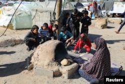 Seorang perempuan Palestina membuat roti sementara anak-anak duduk di sebelahnya, sementara penduduk Gaza menghadapi krisis kelaparan dan melonjaknya kekurangan gizi, di Khan Younis di selatan Jalur Gaza, 24 Januari 2024. (Foto: REUTERS/Arafat Barbakh)