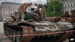 Combat engineers inspect a damaged Russian tank installed as a symbol of war in central Kyiv, Ukraine, June 15, 2023. 