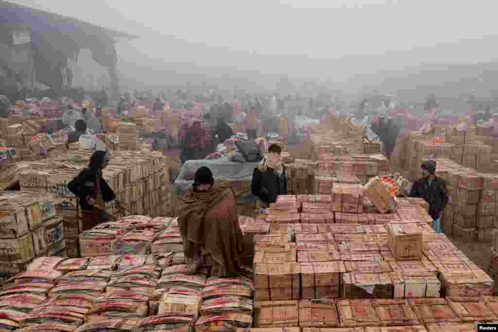 People cover themselves to stay warm during heavy fog, early in the morning at the fruit wholesale market on the outskirts of Peshawar, Pakistan.