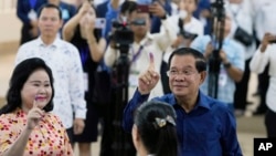Cambodian Prime Minister Hun Sen, right, shows off his ink-stained finger, together with his wife Bun Rany, left, after they cast their ballots at a polling station in Takhmua, southeast of Phnom Penh, Cambodia, July 23, 2023. 
