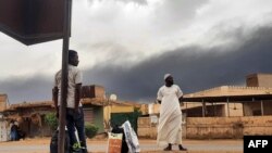 Smoke rises above buildings as people wait on the side of a road with some belongings in Khartoum, June 10, 2023. A 24-hour cease-fire took effect on June 10 between Sudan's warring generals.