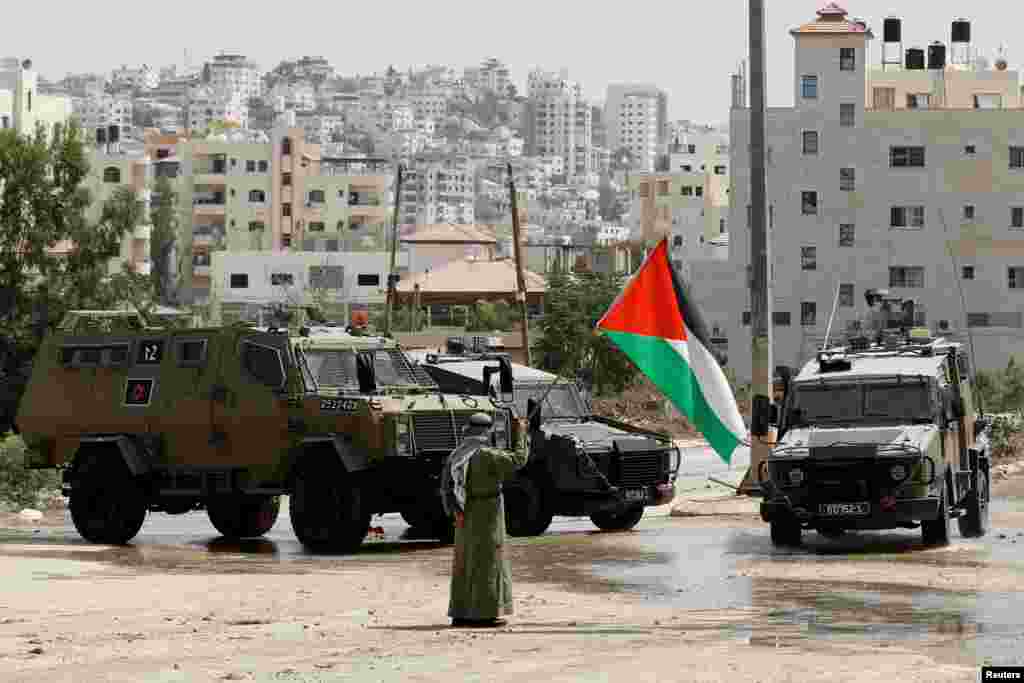 A man holds the Palestinian flag next to Israeli military vehicles during a raid in Tulkarm, in the Israeli-occupied West Bank.