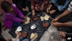 Members of the Abu Jarad family, who were displaced by the Israeli bombardment of the Gaza Strip, eat breakfast at a makeshift tent camp in the Muwasi area, southern Gaza, Jan. 1, 2024.