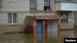 A local resident looks out a window of an apartment building in an area flooded after the Kakhovka Dam breached, in Kherson, Ukraine, June 10, 2023.