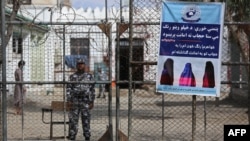 FILE - A Taliban prison security guard stands next to a poster ordering women to cover themselves with a hijab during the distribution of new uniforms ceremony by the Taliban authorities at a prison in Jalalabad, Feb. 5, 2023.