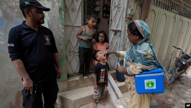 FILE - A police officer stands guard as a health worker administers a polio vaccine to a child at a neighborhood of Karachi, Pakistan, Monday, June 19, 2023.