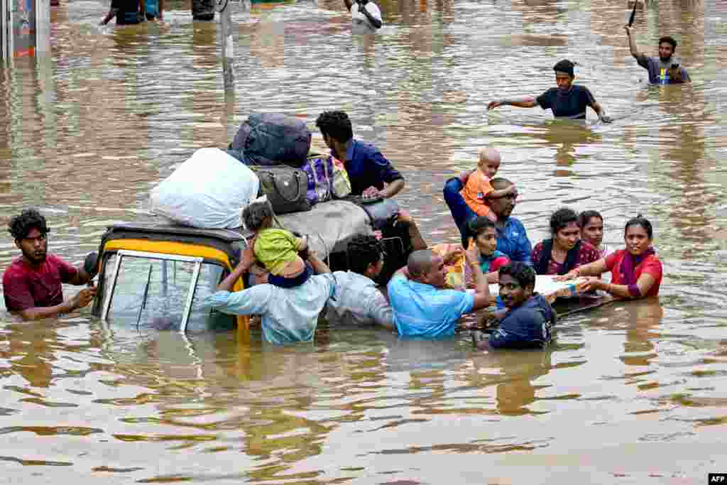 Orang-orang membawa barang-barang mereka saat mengarungi jalanan yang terendam banjir setelah hujan lebat melanda kawasan Vijayawada, India. (AFP)&nbsp;