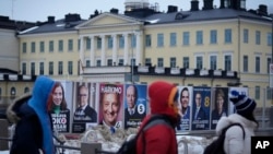 People walk by election posters with the Presidential Palace in the background, in Helsinki, Finland, Jan. 27, 2024, ahead of the Finnish presidential election on Jan. 28.