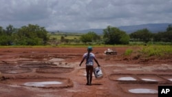 Pi'ilani Taniguchi Butler carries a bucket of wet clay to her family's salt beds on Wednesday, July 12, 2023, in Hanapepe, Hawaii. The salt beds or "loi" are smoothed out using river rocks. The beds are then lined with this rich black clay. (AP Photo/Jessie Wardarski)