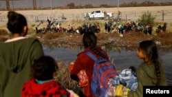 FILE - Migrants seeking asylum in the United States gather on the banks of the Rio Bravo as the Texas National Guard blocks the crossing at the border between the United States and Mexico, as seen from Ciudad Juarez, Mexico, Dec. 5, 2023. 