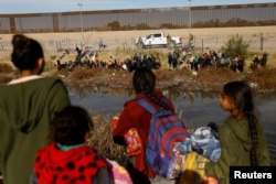 Migrants seeking asylum in the United States gather on the banks of the Rio Bravo river, as the Texas National Guard blocks the crossing at the border between the United States and Mexico, as seen from Ciudad Juarez, Mexico, Dec. 5, 2023.