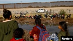 FILE - Migrants seeking asylum in the United States gather on the banks of the Rio Bravo River, as the Texas National Guard waits at the border between the United States and Mexico, as seen from Ciudad Juarez, Mexico, Dec. 5, 2023. 