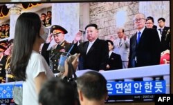 Seorang perempuan berjalan melewati layar televisi di sebuah stasiun kereta api di Seoul, yang menayangkan siaran berita pemimpin Korea Utara Kim Jong Un menghadiri parade militer di Pyongyang untuk memperingati 70 tahun gencatan senjata Perang Korea, Kamis malam (27/7). (AFP)