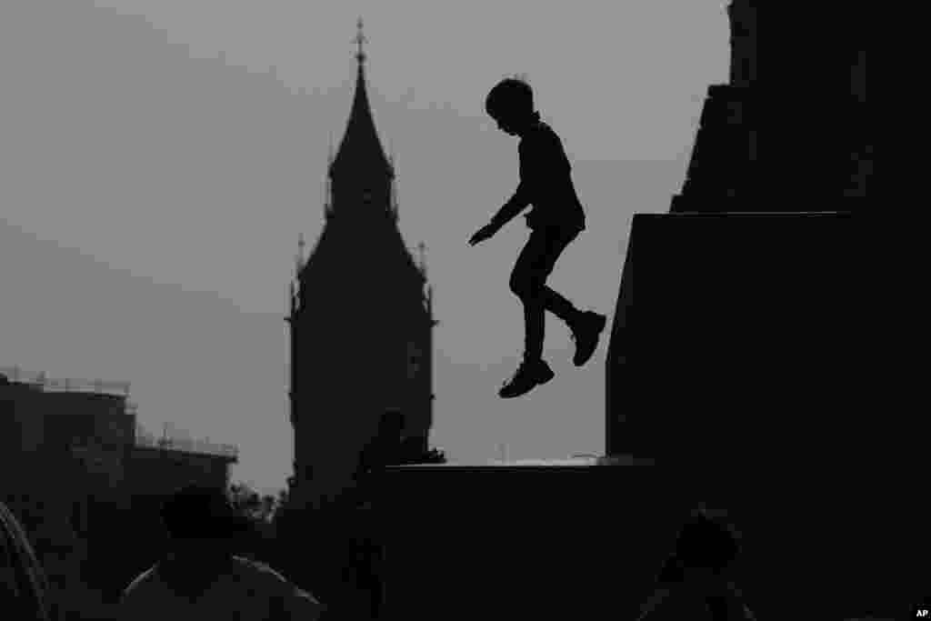 A boy jumps down from a statue at Trafalgar Square with the background of the Elizabeth Tower, known as Big Ben, in London.