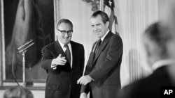 FILE - Menlu AS Henry Kissinger, kiri, memberi isyarat kepada hadirin di Ruang Timur Gedung Putih di Washington DC, disaksikan oleh Presiden Richard Nixon. Saat itu, Kissinger baru saja dilantik sebagai Menteri Luar Negeri AS ke-56.