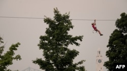 A man ziplines as the Old Port Clock Tower and the Jacques Cartier Bridge are seen in the background with the smoke caused by the wildfires in Northern Quebec in Montreal, Quebec, June 25, 2023.