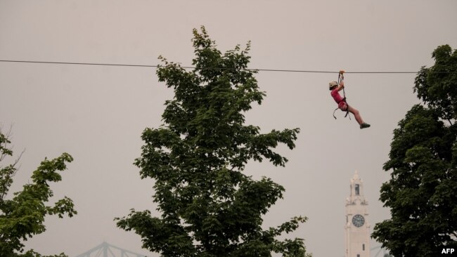 A man ziplines as the Old Port Clock Tower and the Jacques Cartier Bridge are seen in the background with the smoke caused by the wildfires in Northern Quebec in Montreal, Quebec, June 25, 2023.