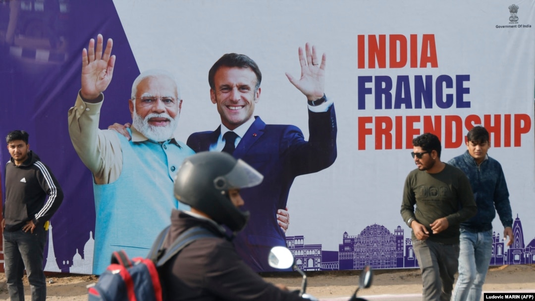 Seorang pria melewati papan reklame bergambar Presiden Prancis Emmanuel Macron (3 kanan) dan Perdana Menteri India Narendra Modi (2 kiri), di Jaipur pada 25 Januari 2024. (Foto: Ludovic MARIN/POOL/AFP)