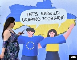 A woman walks past a placard reading "Let's rebuild Ukraine together!" in the center of Ukrainian capital of Kyiv, May 24, 2023.