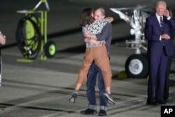 Reporter Evan Gershkovich hugs his mother, Ella Milman, as President Joe Biden, right, looks on at Andrews Air Force Base, Md., following their release as part of a 24-person prisoner swap between Russia and the United States, Aug. 1, 2024.