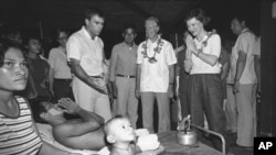 FILE - Rosalynn Carter returns the traditional greeting she receives from a double amputee as she and her husband, former President Jimmy Carter, second from right, visit a hospital at Khao-I-Dang, June 5, 1985. 