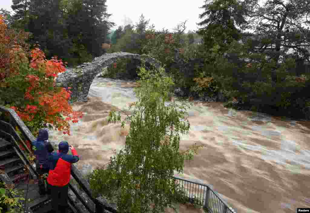 People take pictures of water rushing under the oldest stone bridge in the Highlands at Carrbridge, Scotland, Britain.