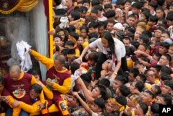 Seorang perempuan berjalan mencoba mendekati kereta berlapis kaca yang membawa Black Nazarene dengan menapaki bahu lautan manusia dalam prosesi tahunan di Manila, Filipina, Selasa, 9 Januari 2024. (AP/Aaron Favila)