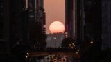 The sun sets as seen between buildings along 42nd Street in New York during a phenomenon known as Manhattanhenge, May 30, 2023.